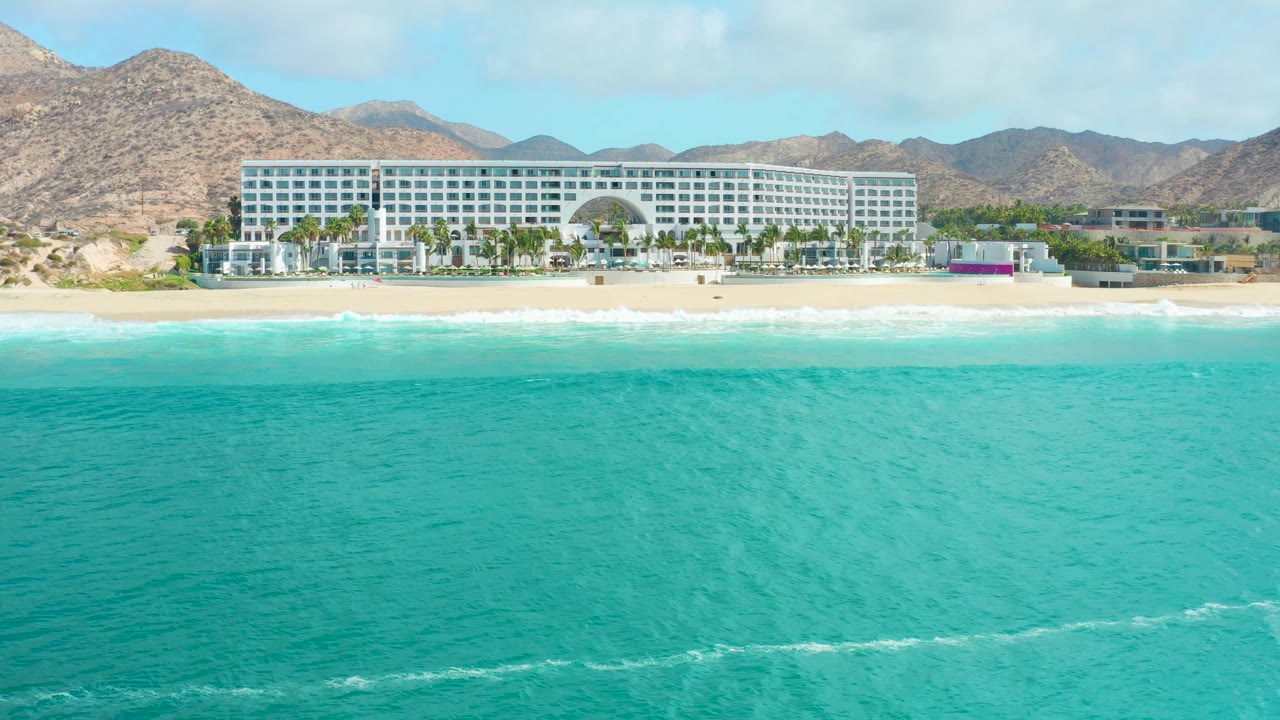 Small white surf line approaching a sandy beach below a hotel.