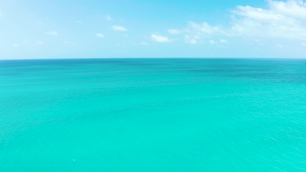 Mid-clip frame shows calm turquoise ocean at Marquis Los Cabos reaching a straight horizon below thin cloud cover, with no visible people.