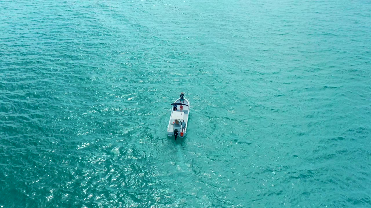 A small white boat remains isolated on blue-green water near Marquis Los Cabos, with darker ripples spreading around the hull and no visible people.