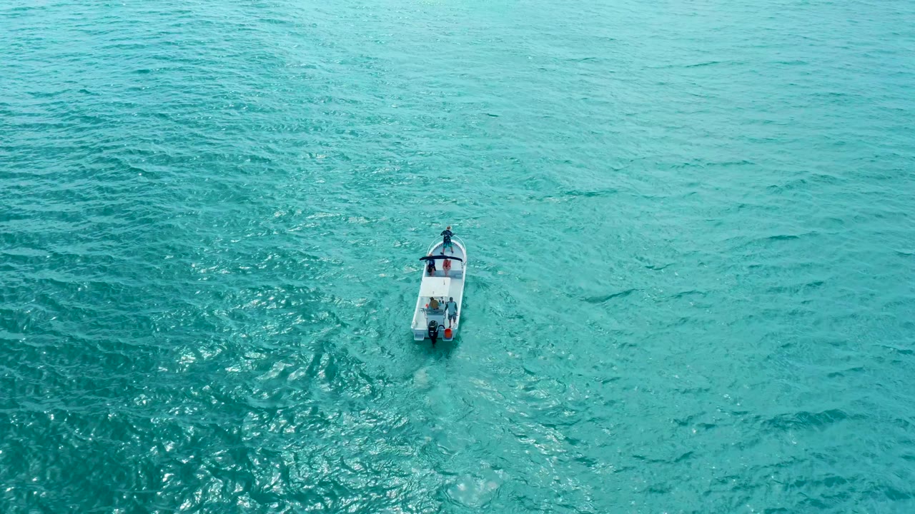 The aerial view near Marquis Los Cabos shows the small vessel slightly farther across the turquoise surface, with sunlit texture and no visible people.