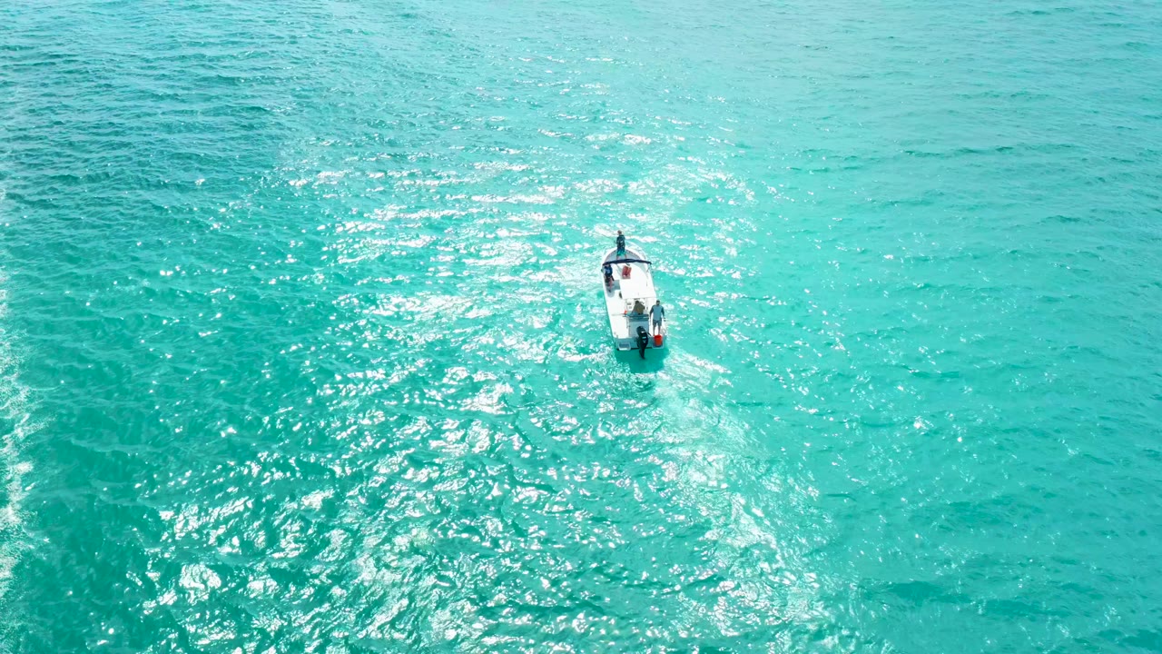 At Marquis Los Cabos in Baja California Sur, a small white boat sits near the upper center of bright turquoise water with sun reflections spreading below it.