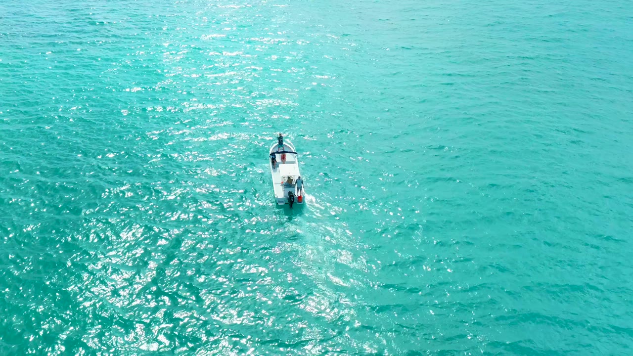 The boat remains near the center of a high overhead Marquis Los Cabos ocean view, with a faint wake trailing behind it and no visible people.