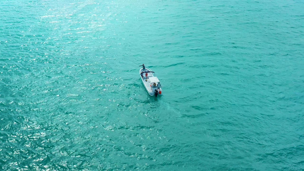 The small boat remains alone in a wide overhead view of bright turquoise water at Marquis Los Cabos, with shimmering highlights and no visible people.