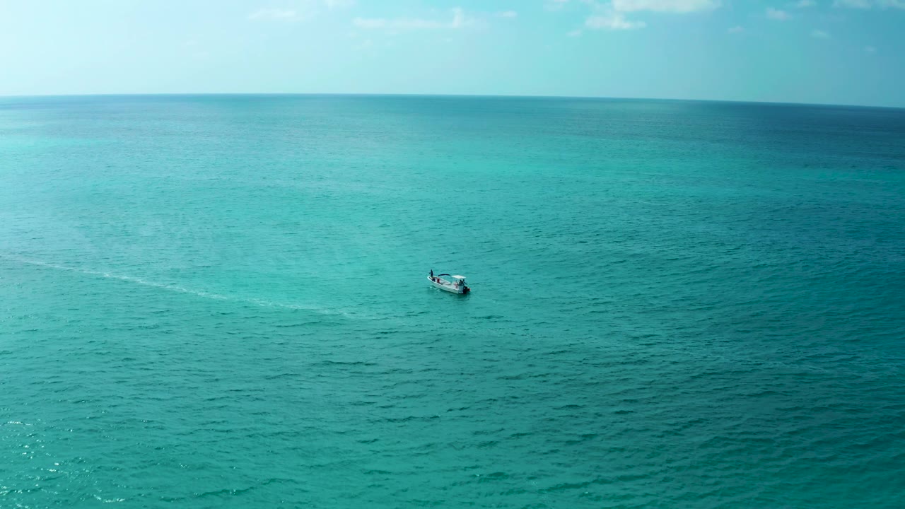 The boat sits slightly farther right in the wide ocean frame near Marquis Los Cabos, with rippled turquoise water, pale sky, and no visible people.