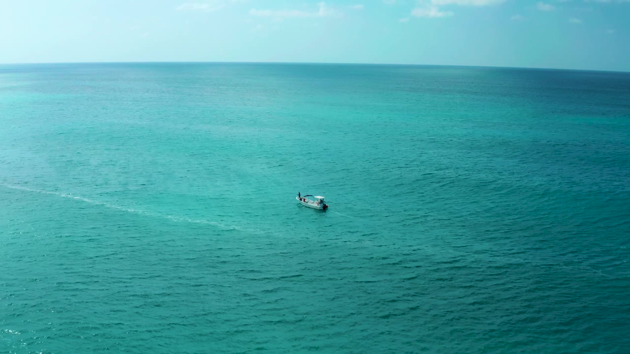 A small boat continues across the blue-green ocean near Marquis Los Cabos, with a longer pale wake line visible across the water and no visible people.