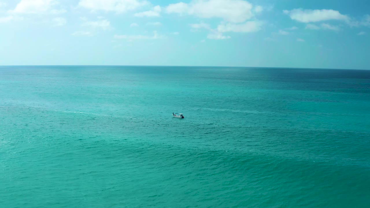 Small boat on turquoise ocean under a pale blue sky.