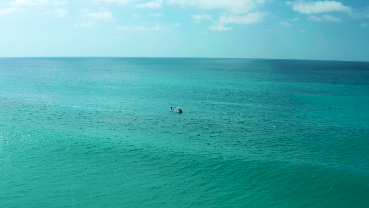 At Marquis Los Cabos in Baja California Sur, a distant small boat crosses the midground of the turquoise sea, with darker blue water near the horizon and no visible people.