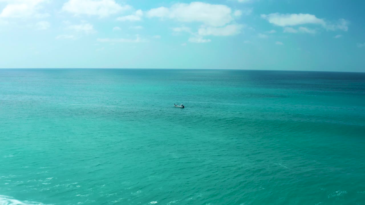 Wide elevated view over calm turquoise water at Marquis Los Cabos after the wave action, with a small boat in the mid-distance, a level horizon, light clouds, and no visible people.
