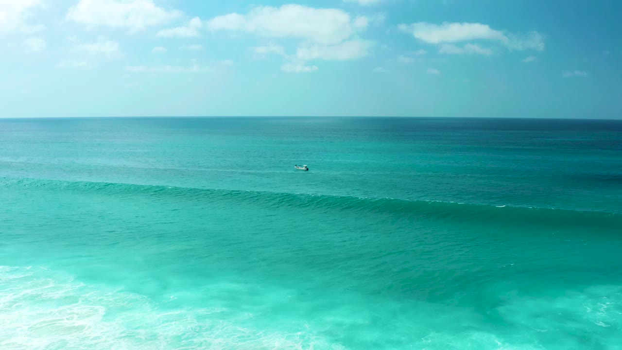 Aerial view at Marquis Los Cabos, Mexico, with turquoise ocean, a dark wave line forming across the lower frame, pale clouds above the horizon, and no visible people.
