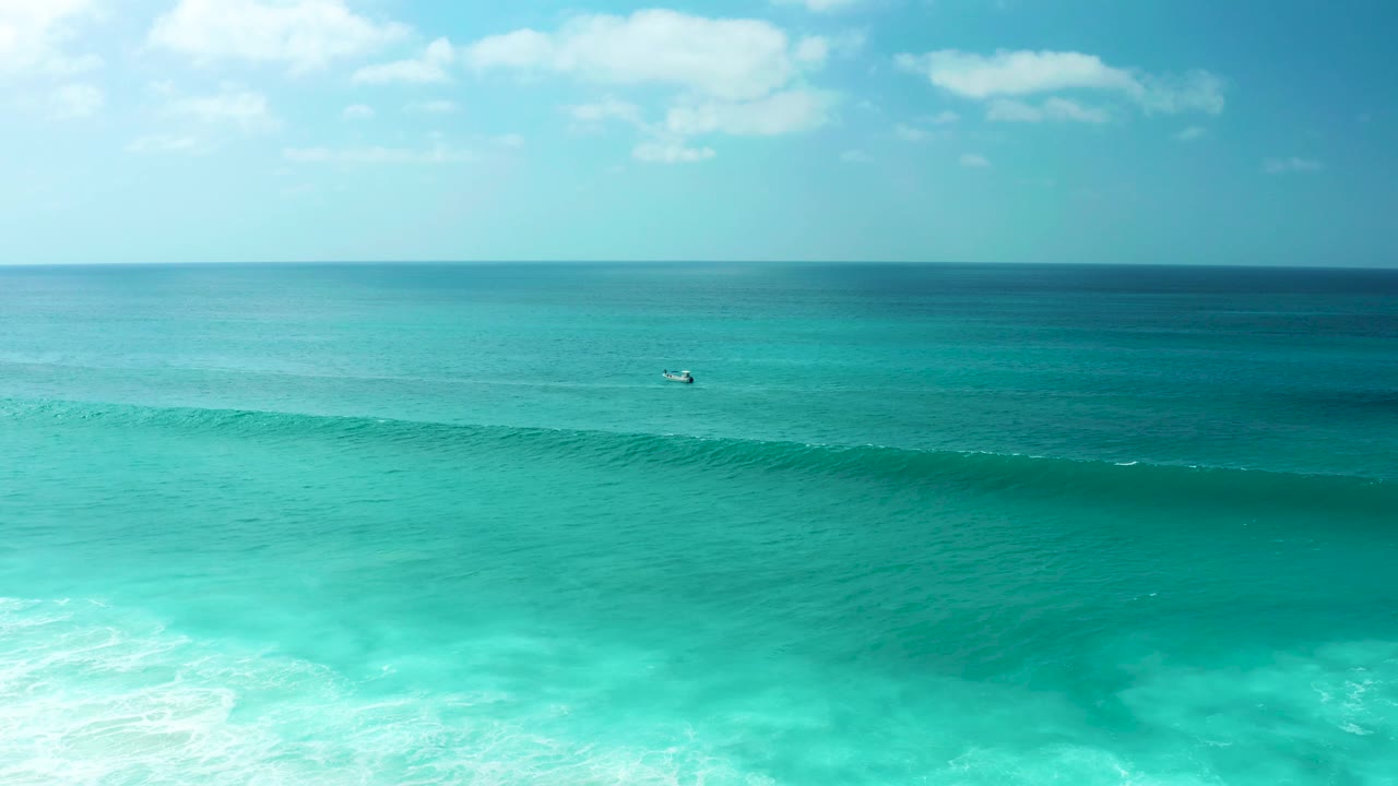 Turquoise sea with a long wave crest and a small distant craft near the horizon.