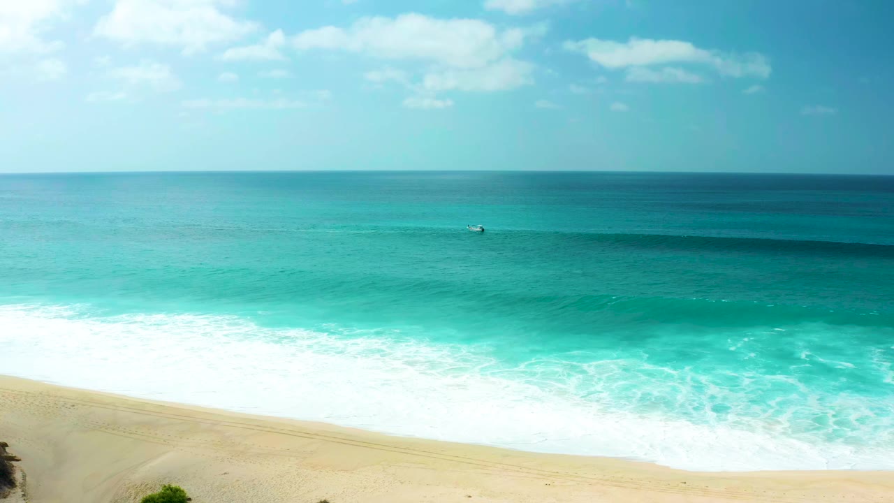 At Marquis Los Cabos in Baja California Sur, turquoise water rolls toward pale sand beneath scattered clouds, with no visible people in the frame.