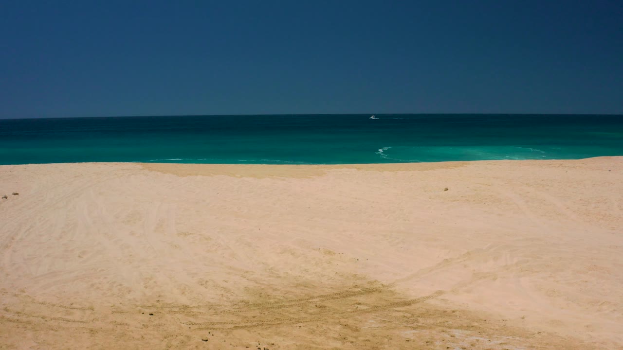 Wide elevated view of sandy beach and turquoise ocean at Dreams Los Cabos, Baja California Sur, Mexico, with small wave marks and no visible people.