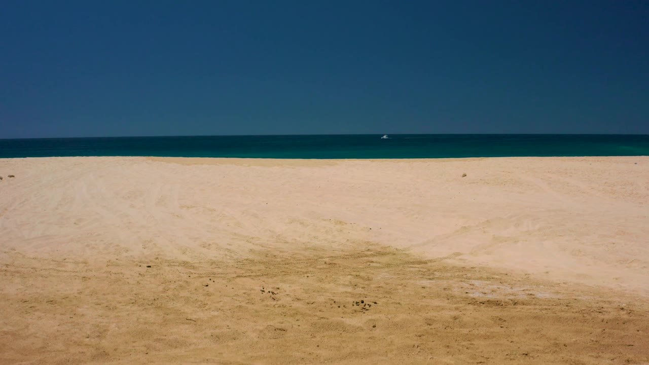 Pale beach and ocean horizon under clear sky.