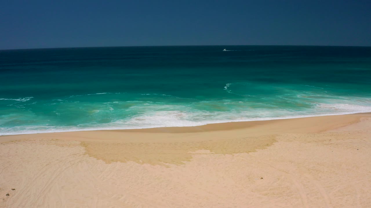 Turquoise waves reaching a sandy beach under a blue sky
