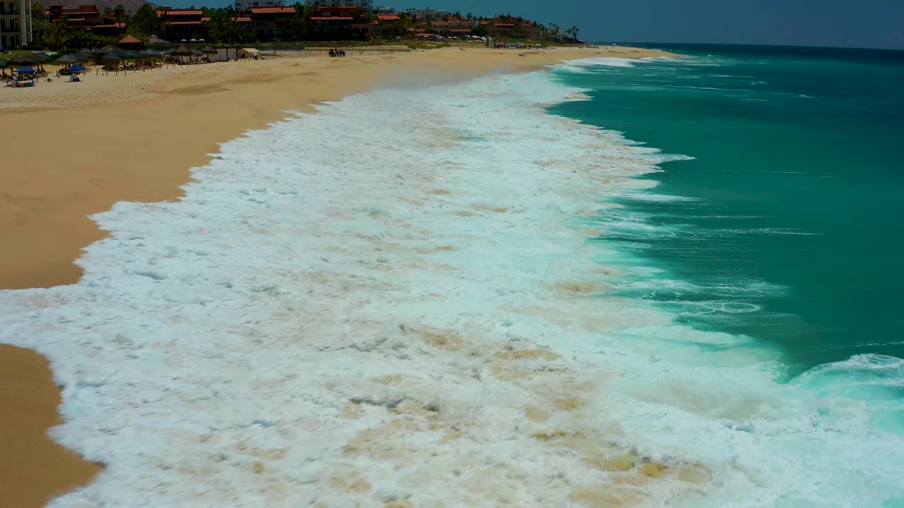 White foam pushes farther over the beach with turquoise water along the right edge.