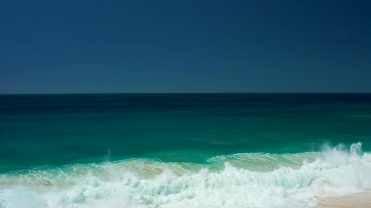 Foamy surf splashing along turquoise water near shore.