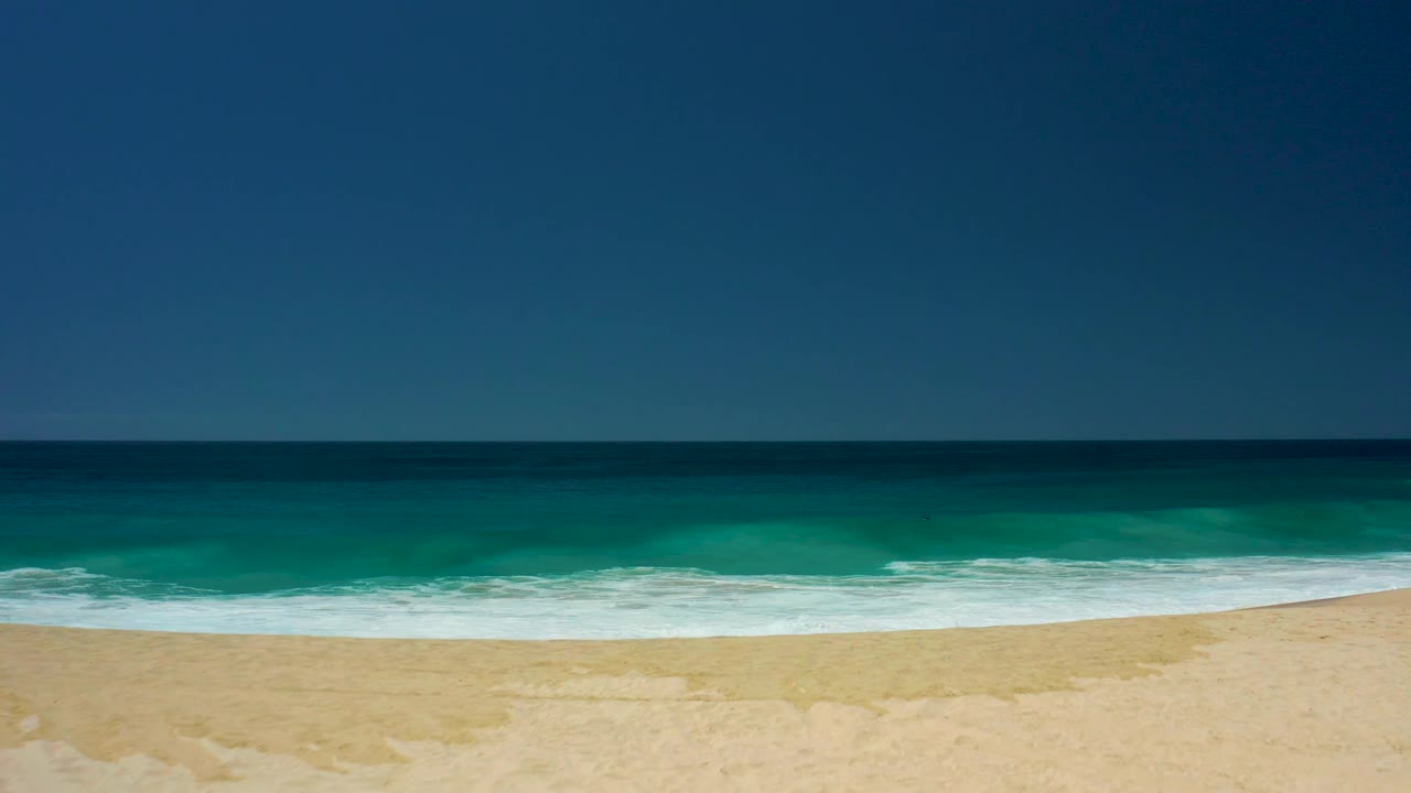 Ocean waves begin foaming toward the sandy beach.