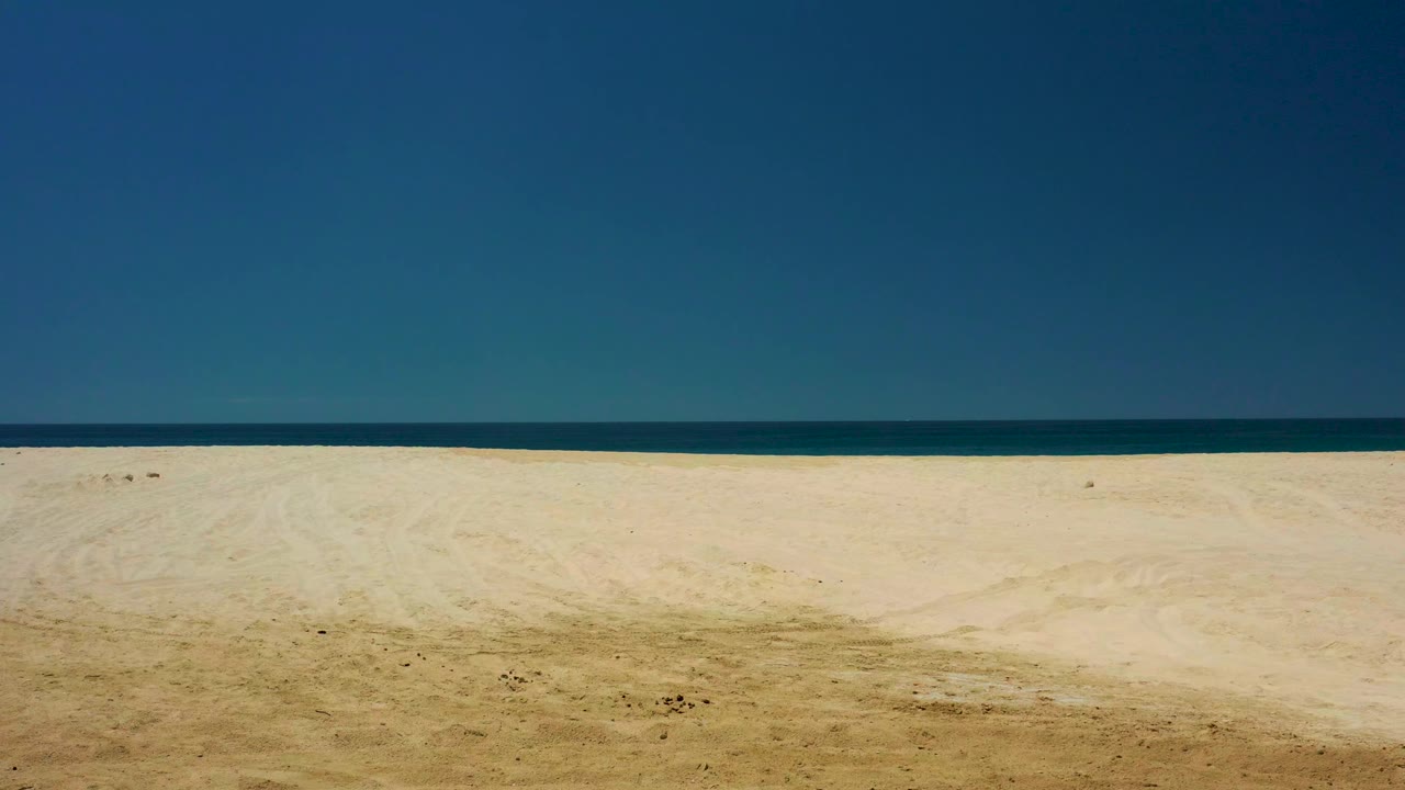 Wide sandy beach under clear blue sky with calm ocean on the horizon.