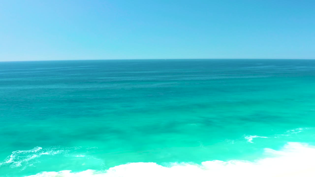 The second frame holds a straight blue horizon over turquoise sea as a bright band of shore foam spreads across the lower right, with no visible people.