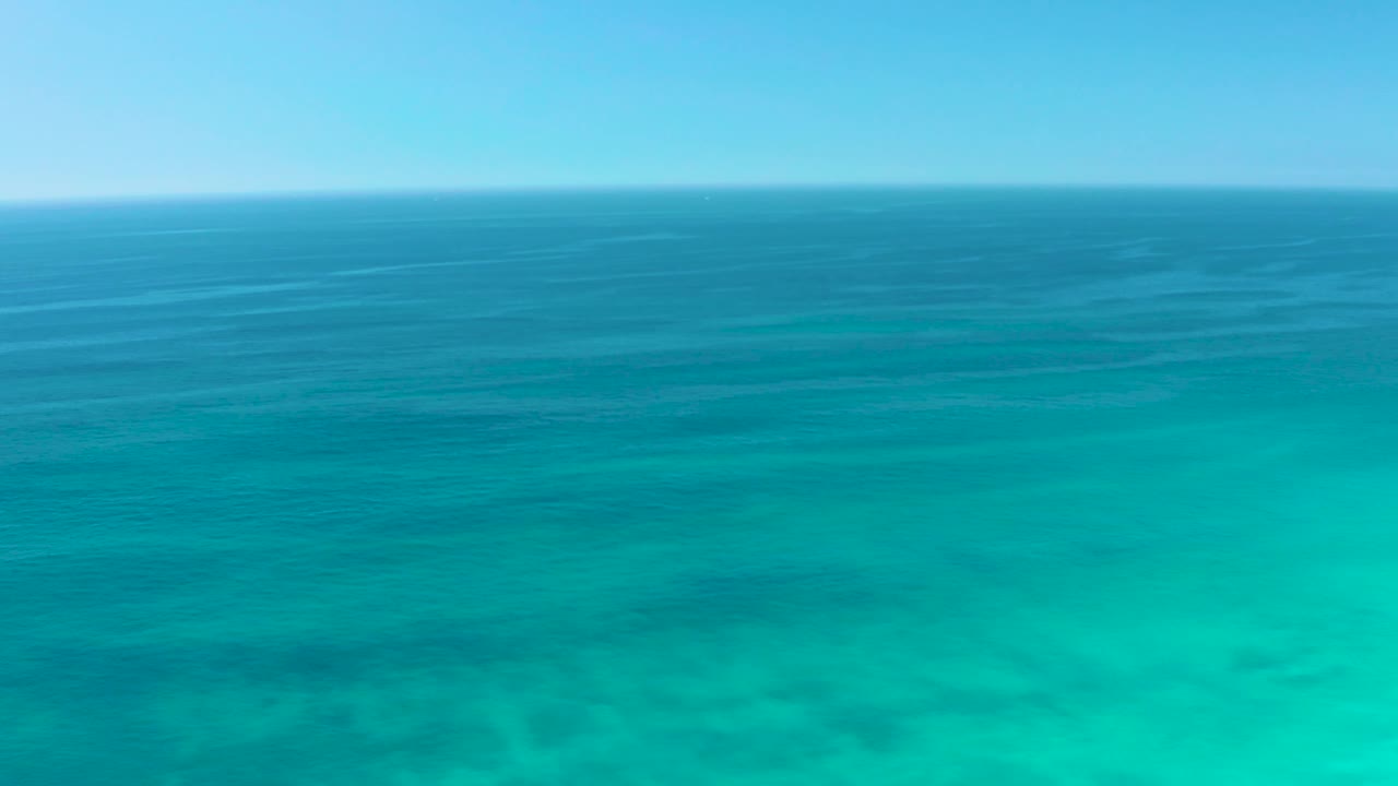 Shallow turquoise water at Dreams Los Cabos shows faint seabed texture beneath darker surface bands, with no visible people.
