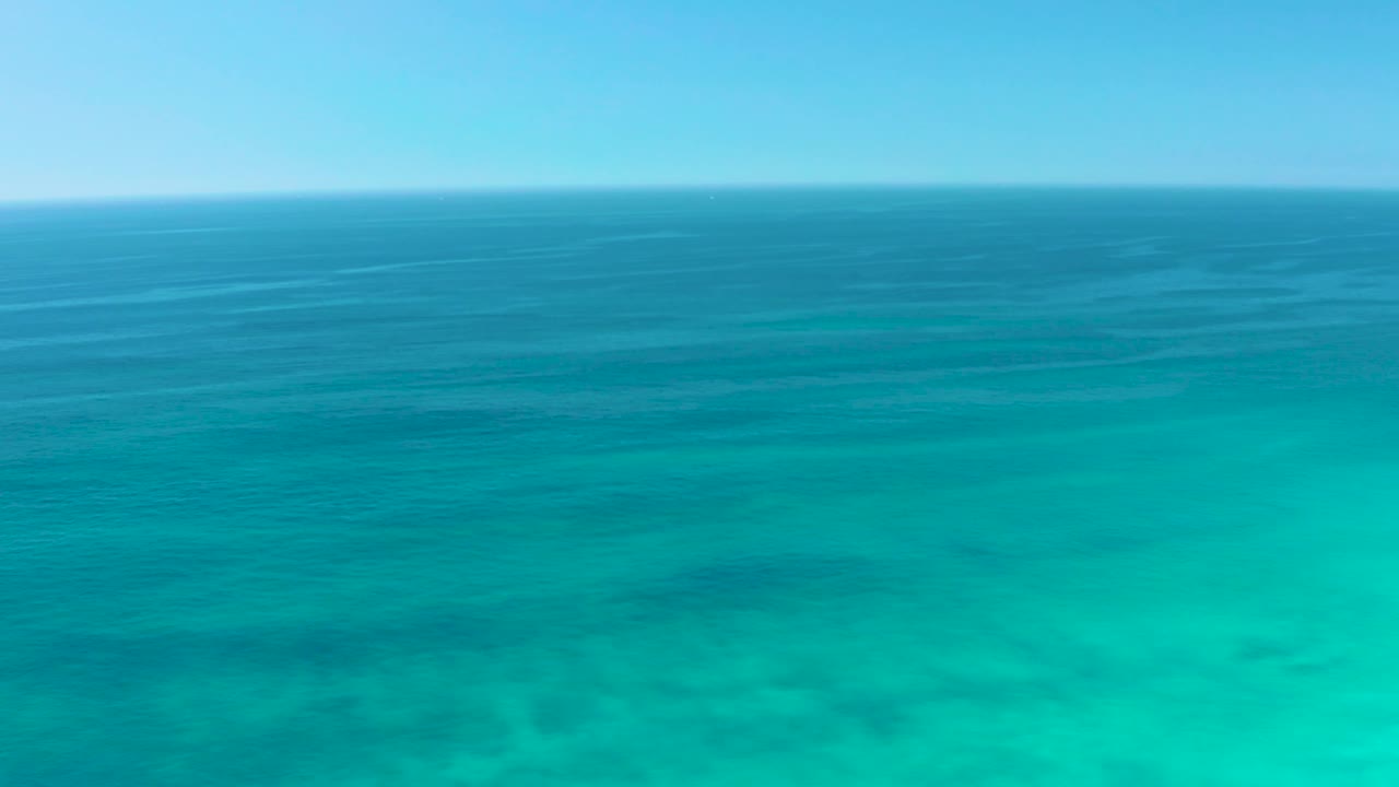 A high ocean view at Dreams Los Cabos holds a straight horizon over layered blue and turquoise water, with no visible people.