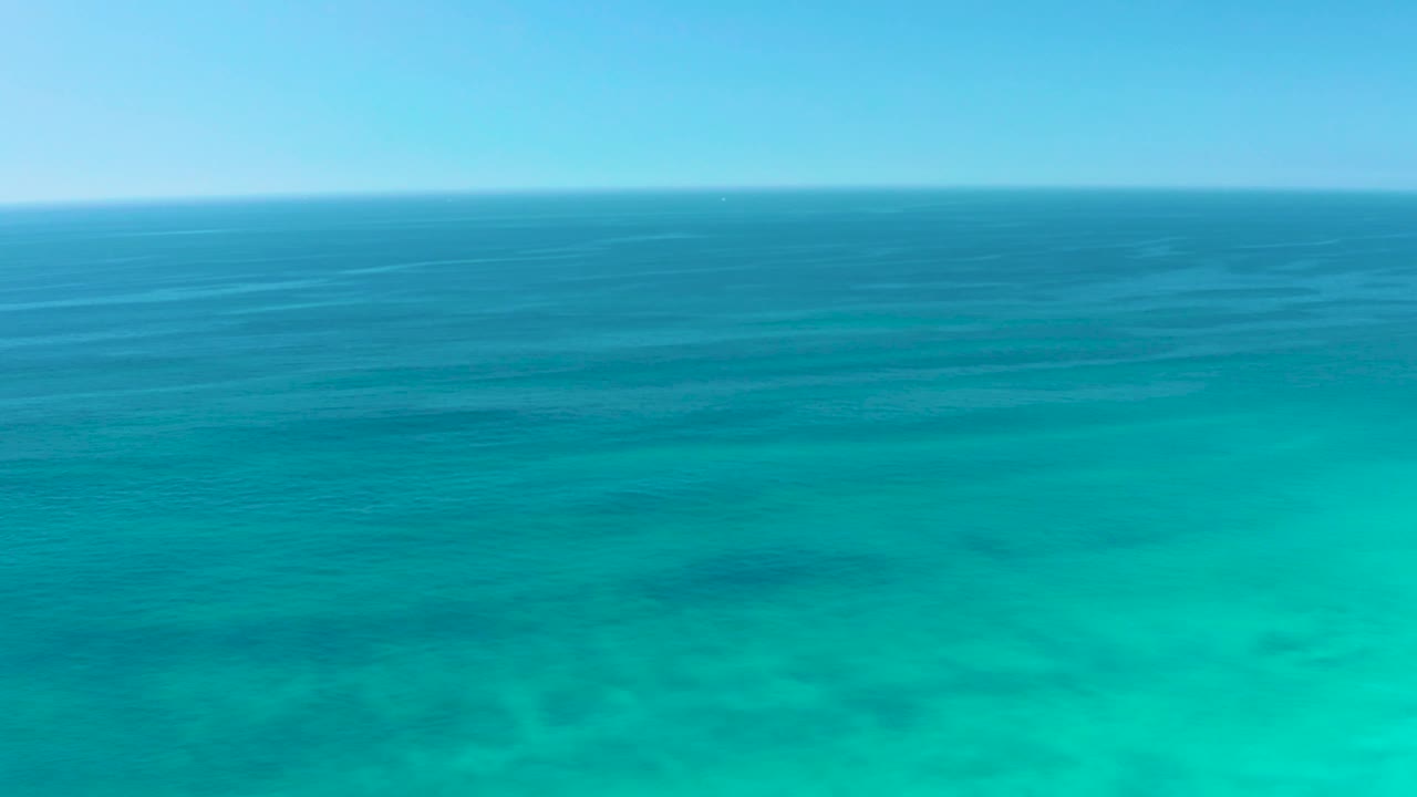 The Dreams Los Cabos ocean appears brighter turquoise in the foreground, with soft ripple lines and faint seabed patches, with no visible people.