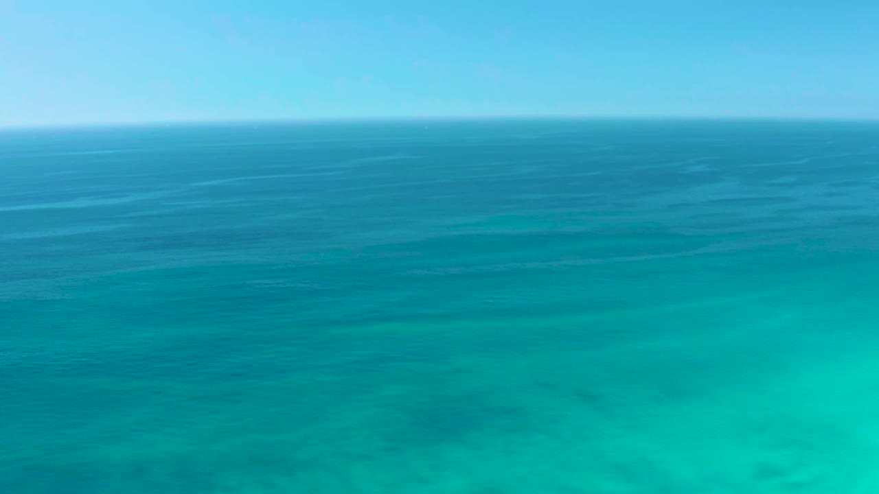 Early frame over Dreams Los Cabos ocean water, showing a broad band of blue sea above clearer turquoise shallows with soft ripple lines and no visible people.