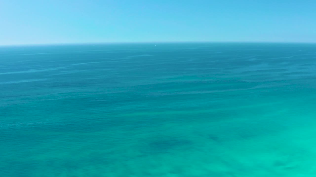 Mid-clip frame of Dreams Los Cabos water, where calm blue ocean fades into a wide turquoise foreground with faint underwater patterns and no visible people.