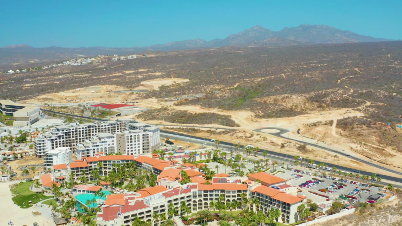 Elevated resort view with pool, parking lot, road, and mountains.