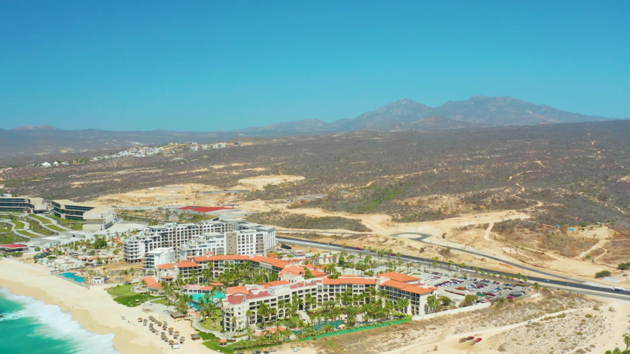Wide aerial view of beachfront resort, sandy beach, road, desert hills, and mountains