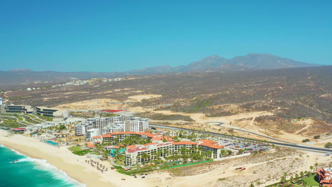 Beachfront resort and turquoise water seen from above with road and mountains inland.