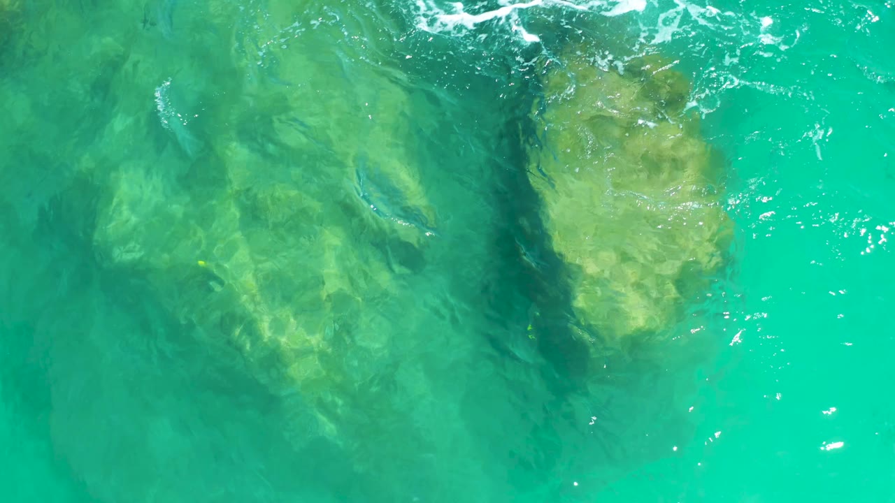 At 0:01, the underwater rocks sit slightly lower in frame beneath green-blue water, with thin white foam at the top and no visible people.