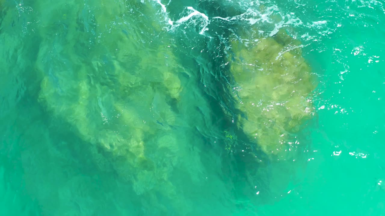 At Dreams Los Cabos, two pale underwater rock areas appear separated by darker water, with bright ripples and foam along the upper edge and no visible people.