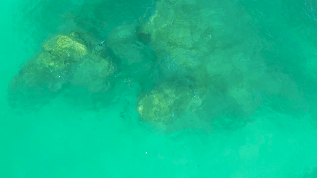 Turquoise ocean water ripples over clustered submerged rocks at Dreams Los Cabos, with brighter green highlights and no visible people.
