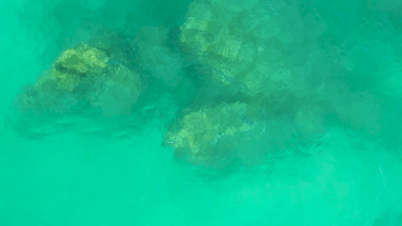 An overhead frame of clear turquoise water at Dreams Los Cabos shows darker submerged rocks near the upper area and no visible people.