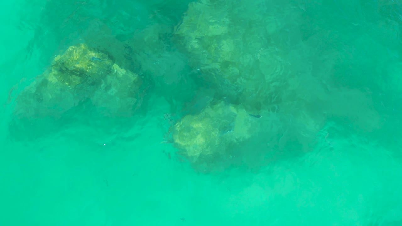 Submerged rocks appear through teal water at Dreams Los Cabos, with surface movement softening their edges and no visible people.