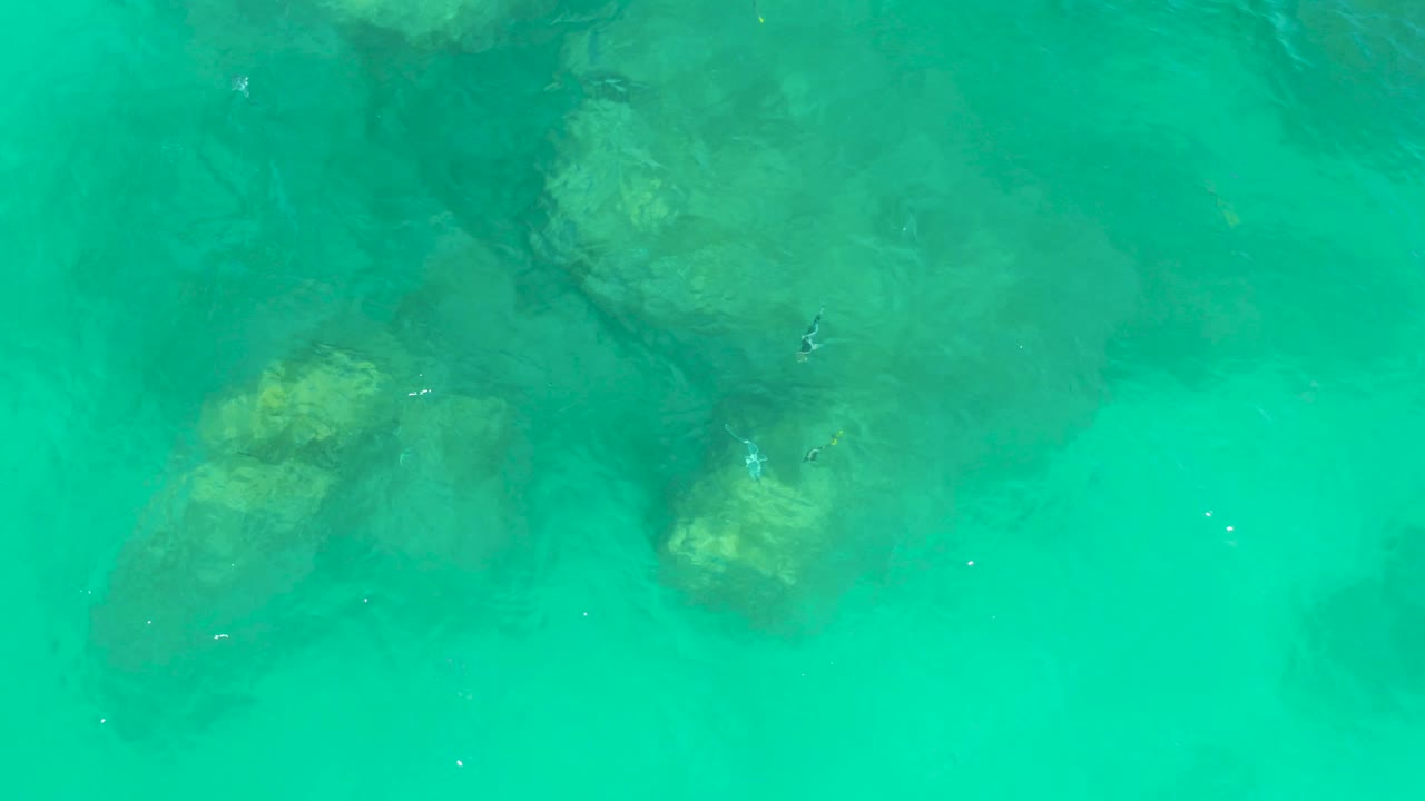 At Dreams Los Cabos, submerged rocks remain visible through turquoise water while darker ripple bands pass across the surface, with no visible people.