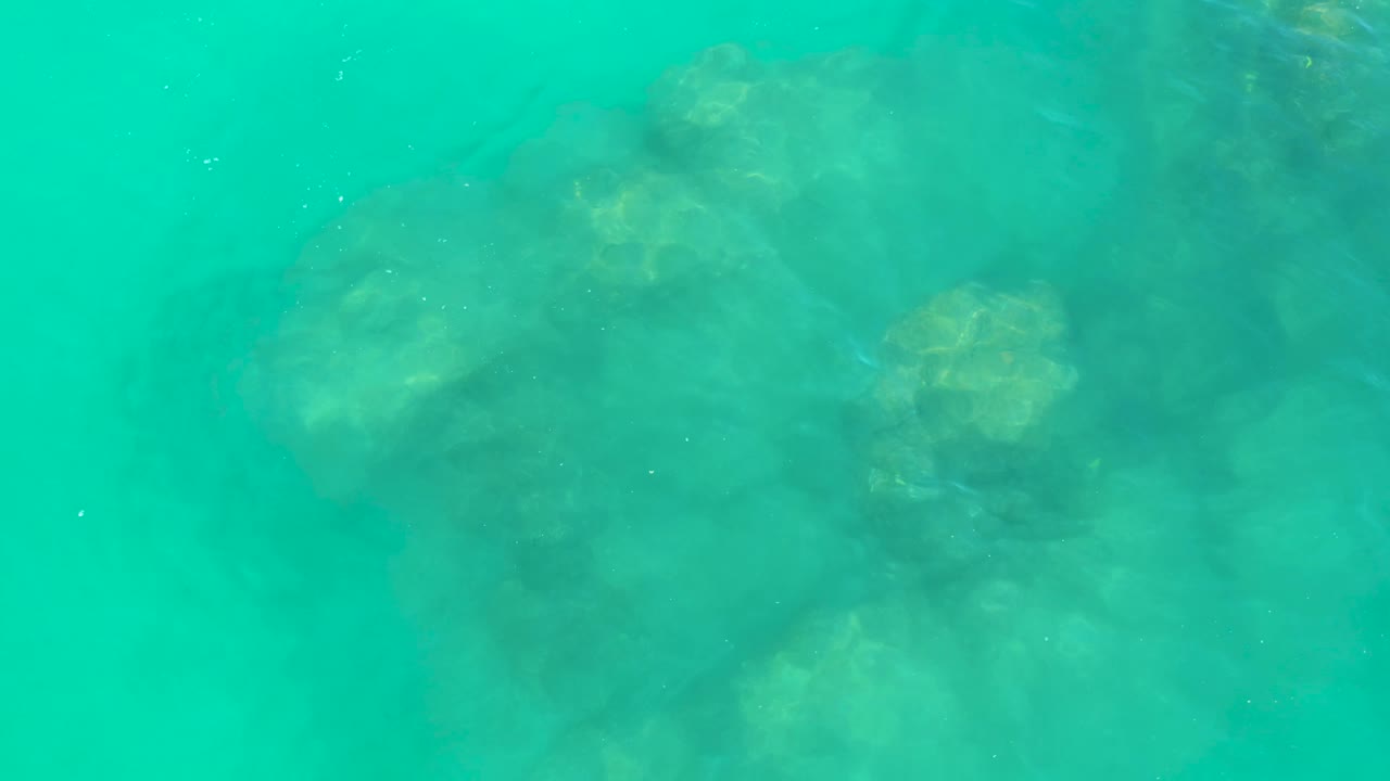 Turquoise ocean water at Dreams Los Cabos shows darker submerged rock clusters beneath a lightly rippled surface with no visible people.
