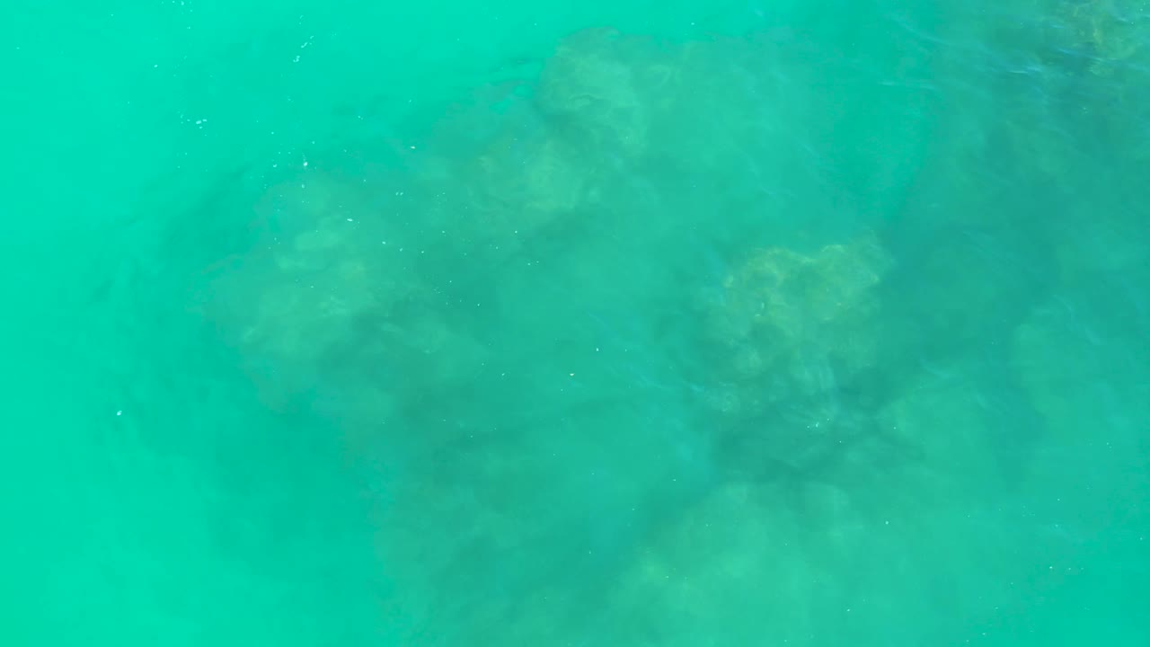 A full-frame overhead look at Dreams Los Cabos water shows soft submerged rock shapes under turquoise ripples and no visible people.