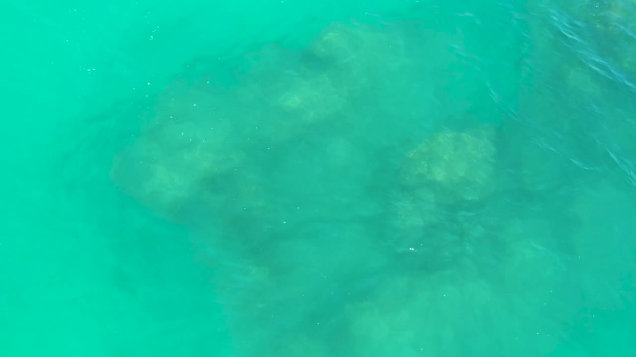 Overhead view of clear turquoise water at Dreams Los Cabos with dark submerged rocks visible below and no visible people.