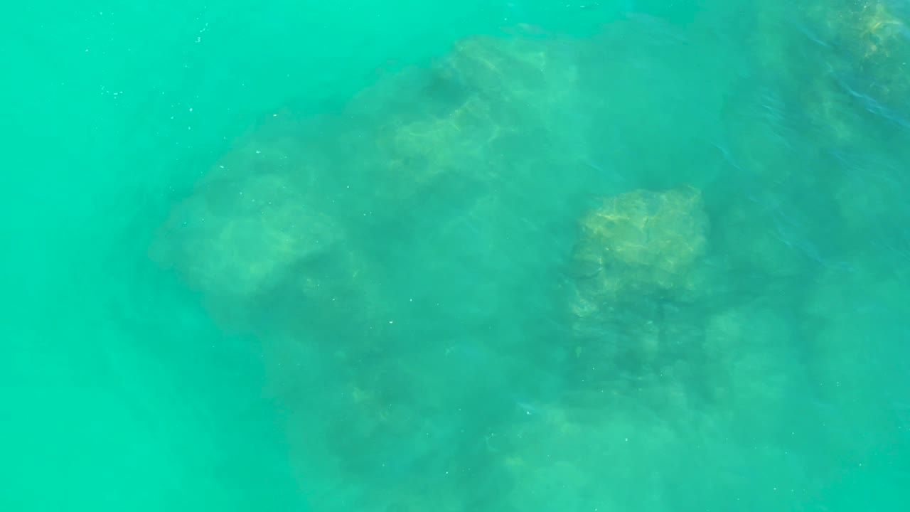Top-down view of turquoise ocean water over clustered submerged rock formations at Dreams Los Cabos, with no visible people.
