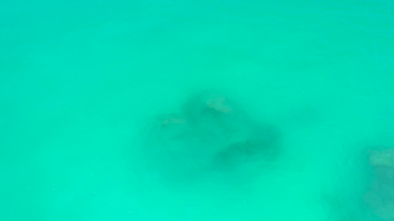 A stingray glides across a pale sandy seabed in turquoise water at Dreams Los Cabos, with a darker patch near its body and no visible people.
