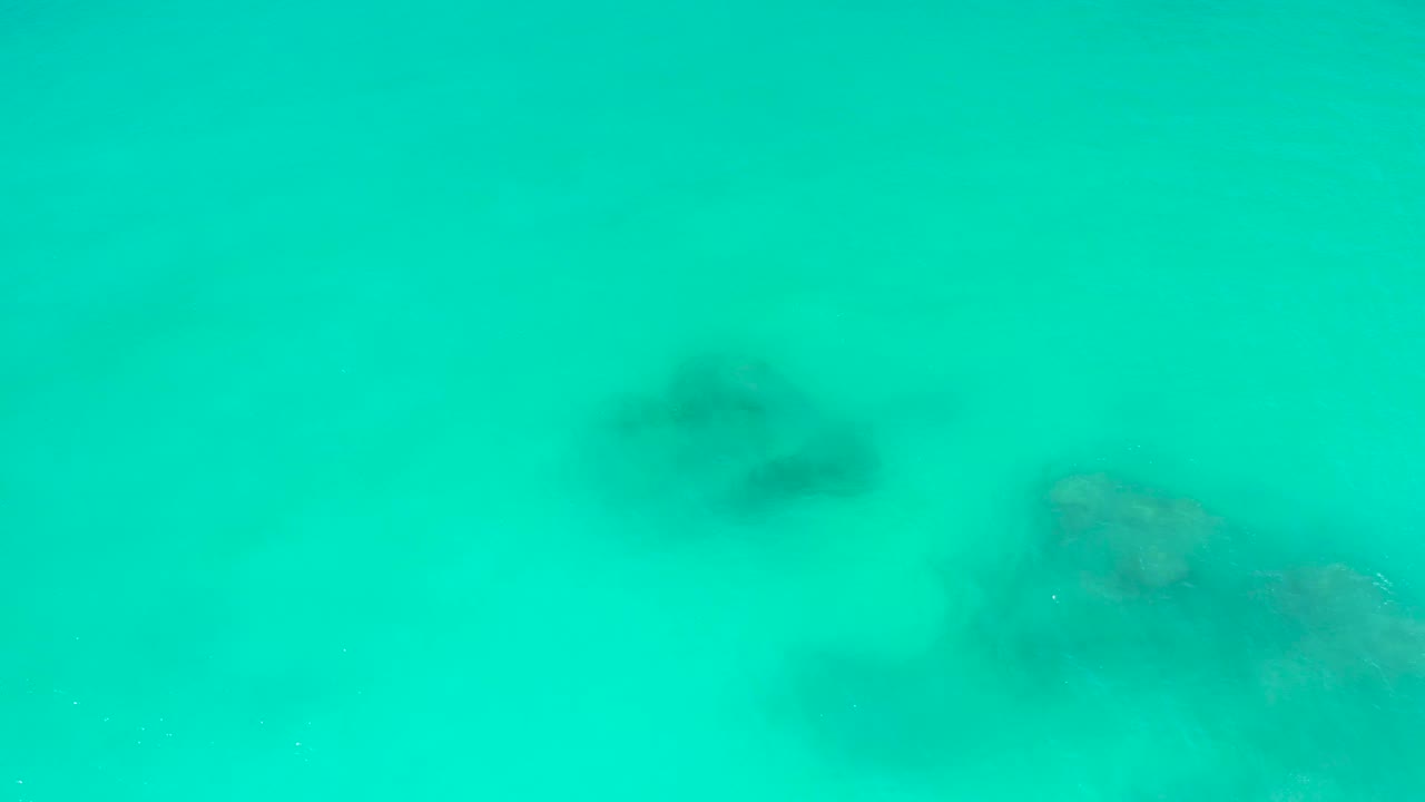 Turquoise underwater frame from Dreams Los Cabos with darker blurred rocks left of center and a larger rocky formation along the lower right, no visible people.