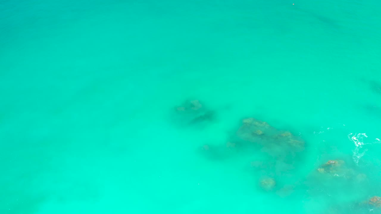 Turquoise shallow water at Dreams Los Cabos shows a cluster of submerged rocks near the lower right, with no visible people.