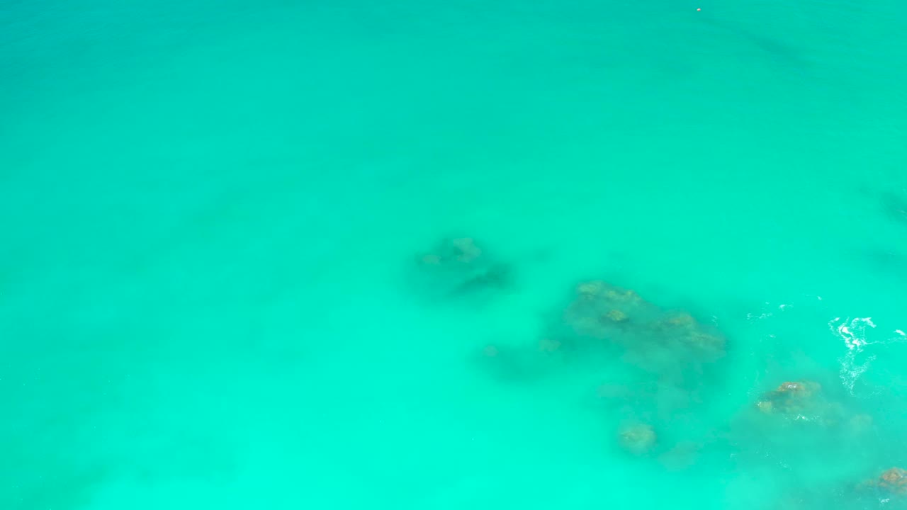 Clear blue-green water at Dreams Los Cabos reveals darker submerged rock shapes through the shallow water, with no visible people.