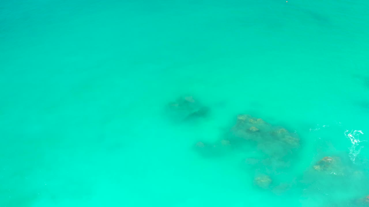 A submerged rock cluster sits under bright turquoise water at Dreams Los Cabos, with a small patch of white surface ripple and no visible people.
