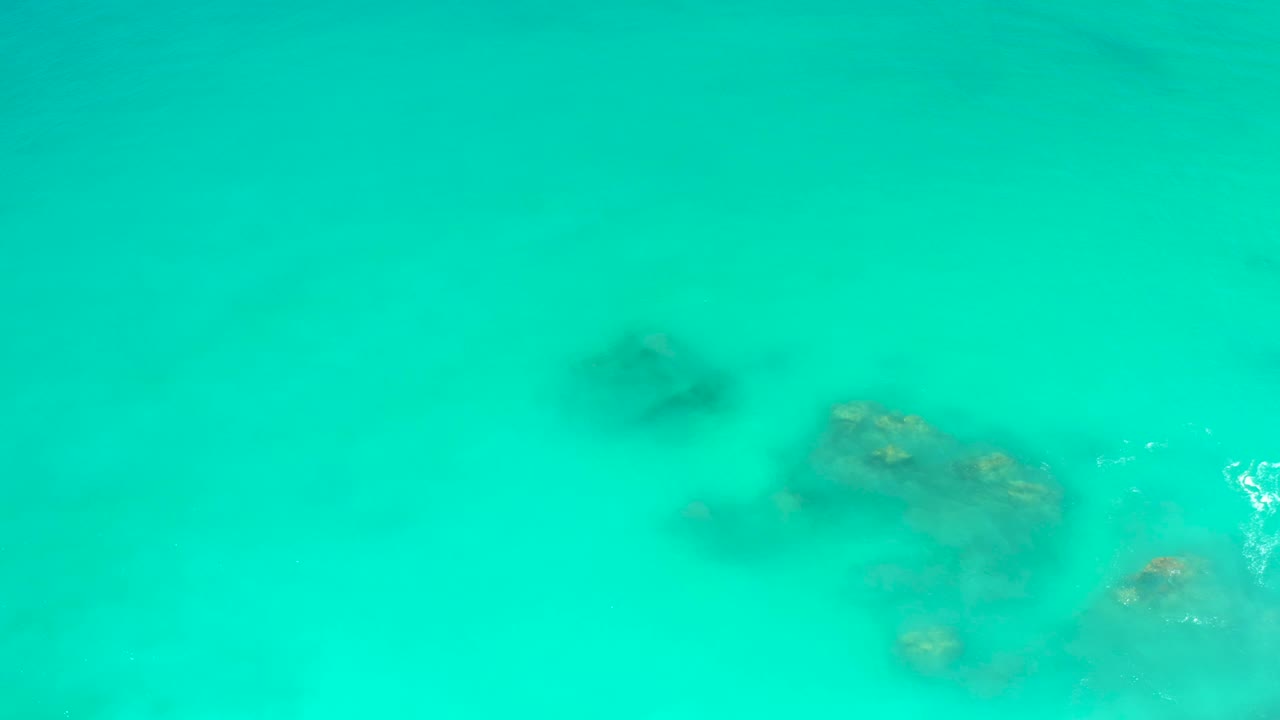 Shallow turquoise water at Dreams Los Cabos covers scattered rocky seabed patches, with the clearest rock detail toward the lower center and no visible people.