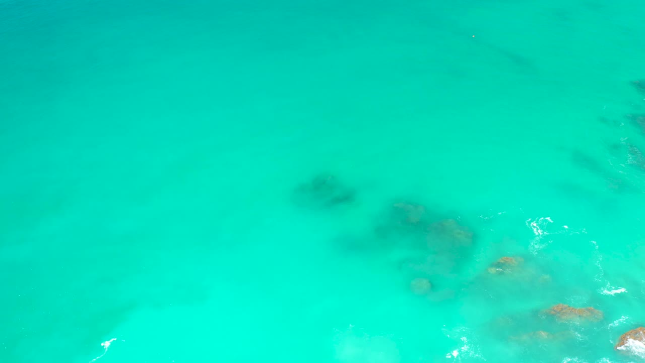Turquoise water at Dreams Los Cabos reveals clustered submerged rocks toward the lower right, with small white foam marks and no visible people.
