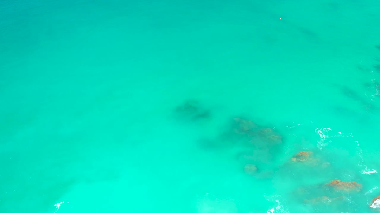 Overhead view of shallow turquoise water at Dreams Los Cabos with shadowy rock patches under the surface and no visible people.