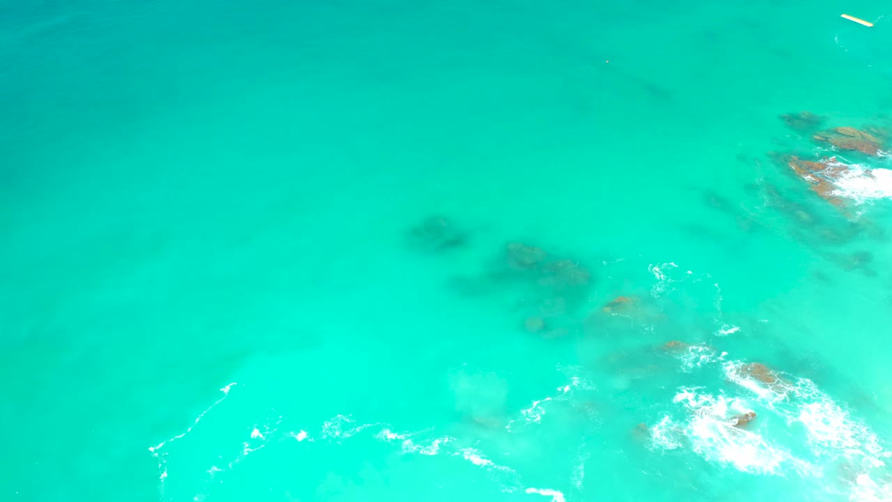 Aerial view at Dreams Los Cabos of turquoise water over rocky seabed, with white foam breaking near the lower edge and no visible people.